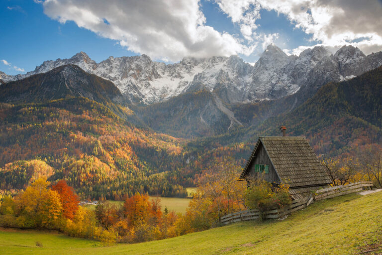 Autumn colours at the fairytale cottage in Srednji Vrh village with the Julian Alps behind, near Kranjska Gora, Slovenia