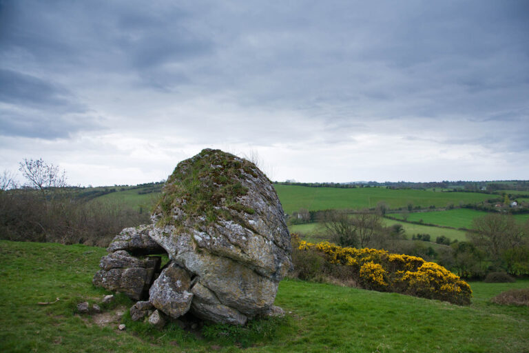 The stone of the Divisions (AKA the Cat Stone) on the Hill of Uisneach in County Meath is is possibly the most signifcant ancient monument in the whole country. Firstly, legend say that this is the burial place of Queen Eriu, Queen of the Tuatha de Danann (A powerful, magical race that inhabited Ireland before the Celts). She was defeated and mortally wounded in a battle with the Celtic King, Amergen granted her a dying wish. He promised her that the island would bear her name forever – The Gaelic name Eriú was later changed by the Vikings into “Eriú’s Land”, or Ireland. This 30-ton stone looks more like a giant bolder that has been cracked into several pieces. The splits are believed to represent the ancient divisions of Ireland. A book called Beneath the Shadow of Uisneach, says that it was from here that the five ancient provinces of Ireland met, symbolising this as the centre of Ireland. The stone’s Irish name depicts this: Ail na Mireann (“Stone of the Divisions”). The division were first made by the Fir Bolg. It is on this hill that the first fire was lit for the ancient festival of Bealtaine. It was said that a fire lit at the summit here could be seen all over Ireland, and that all fires were lit from this one. This hill was also the gathering place of the kings of Ireland.